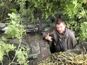 Український військовий біля бронетехніки в густій літній рослинності на фронті