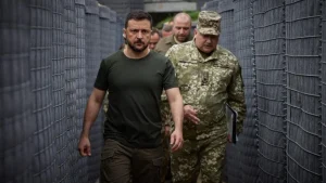 Президент Володимир Зеленський у військовому одязі йде з генералом коридором захисних сіток на Запорізькому напрямку фронту.