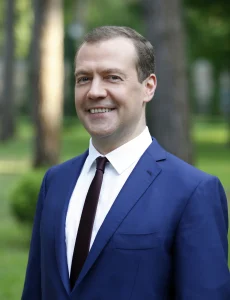 Дмитро Мєдвєдєв у синьому костюмі посміхається на тлі дерев