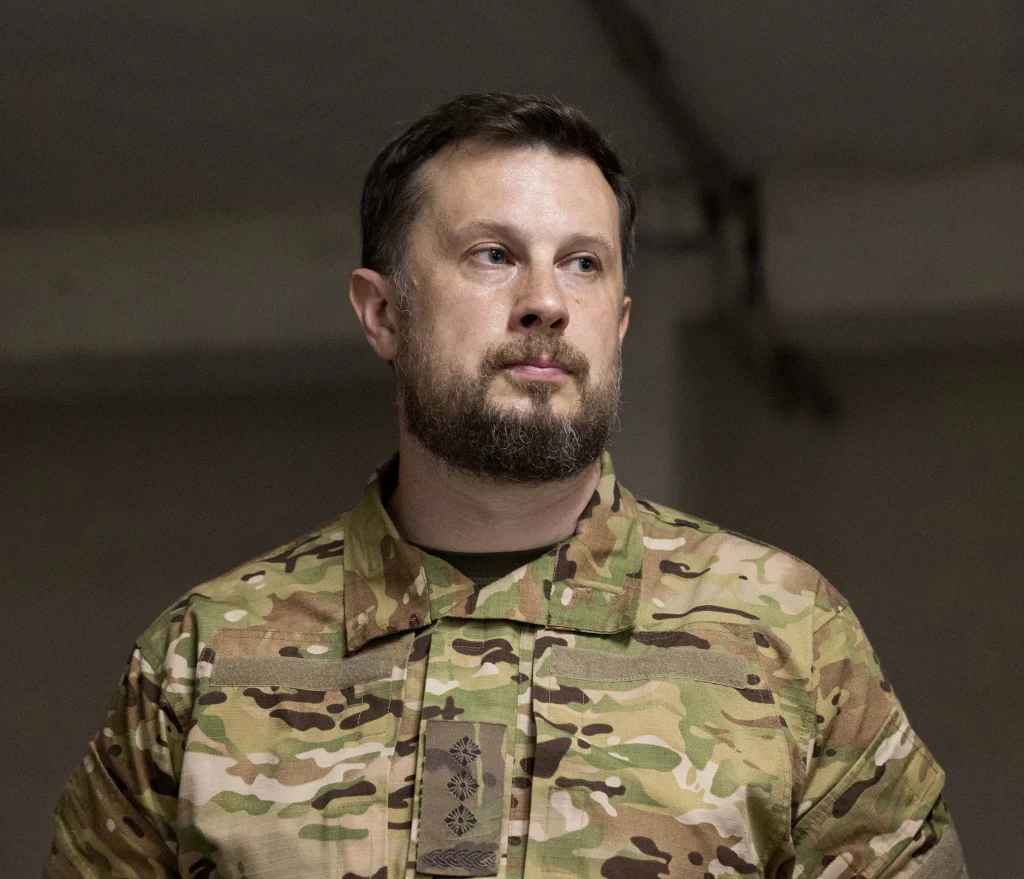 Бородатий чоловік у камуфляжній військовій формі з відзнаками дивиться вбік