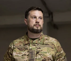 Бородатий чоловік у камуфляжній військовій формі з відзнаками дивиться вбік