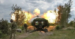 Пограничники у замаскированной артиллерийской установки во время выстрела среди деревьев
