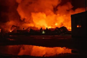 Пожежники на тлі величезної нічної пожежі з димом і уламками
