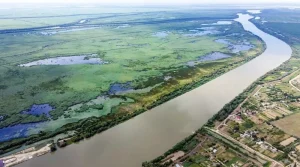 Аерофотознімок широкої річки з болотистими луками та прибережним селом