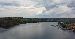 Панорамный вид на реку Днестр с зелёными склонами, лодками у берега и домами под облаками